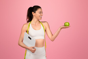 Wall Mural - Smiling fitness-oriented woman with a measuring tape over her shoulder holding a scale