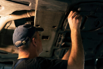At a service station a car mechanic inserts metal panel under the car