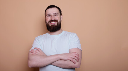 Wall Mural - man with a beard is smiling and wearing a white shirt. He is standing in front of a tan wall