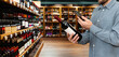 © Barillo_Images - Man in casual clothes customer in liquor store scans e-label on wine bottle using his smartphone.