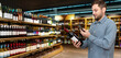 © Barillo_Picture - Man in casual clothes customer in liquor store scans e-label on wine bottle using his smartphone.
