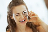 Fototapeta Paryż - Young woman using eyelash curler in bathroom