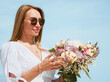 Joyful Young Woman Holding a Bouquet of Flowers on a Beach with Blue Sky Background