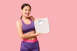 Young woman in sportswear and with weight scales on pink background. Slimming concept