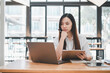 © Satori Studio - A contemplative young adult woman working diligently on a laptop while holding a clipboard in a modern cafe setting.