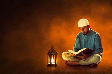 Poster - Young asian muslim man with beard reading holy book quran in the mosque at dark night