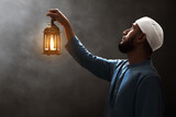 Fototapeta Na ścianę - Young asian muslim man with beard holding arabic lantern looking up on dark background at night