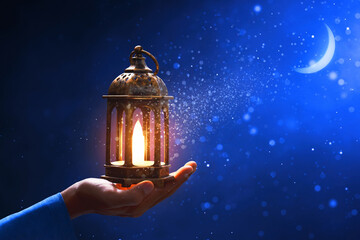 Canvas Print - Hands of young asian muslim man holding shiny arabic lantern at blue night sky with stars and crescent moon, with glitter and sparkle effect