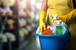 A woman standing with a bucket and cleaning products in her hands on a blurred background.