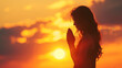 canvas print picture - Young woman praying on the background of the setting sun