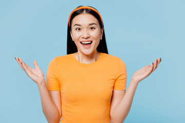 Wall Mural - Young smiling cheerful happy woman of Asian ethnicity wear orange t-shirt casual clothes look camera spread hands isolated on plain pastel light blue cyan background studio portrait Lifestyle concept