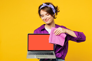 Poster - Young IT woman wear purple shirt hold basin with detergent bottles do housework tidy up wiping blank screen laptop pc computer with dust cloth isolated on plain yellow background Housekeeping concept