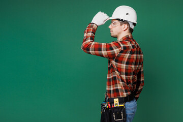 Poster - Side profile view young employee laborer handyman man wears red shirt tipping hardhat hat isolated on plain green background. Instruments accessories for renovation apartment room Repair home concept