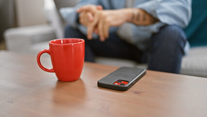 Poster - Intimate glance at a man's hands, sitting on a sofa, engrossed with his cellphone, in the cozy home interior. nearby, on the table, sits a cup of his favored beverage.