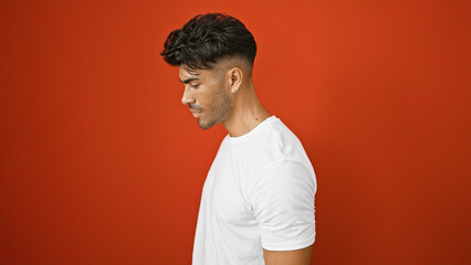 Wall Mural - Handsome young hispanic man with a beard posing in a white shirt against an isolated red background.