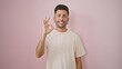 © Krakenimages.com - Cheerful young hispanic man confidently flashes an ok gesture, standing isolated over a suave pink background, radiating positivity, a heartwarming smile, and casual-fashion coolness.