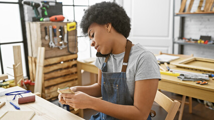 Wall Mural - African woman counts money while talking on phone in a carpentry workshop