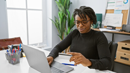 Sticker - A young african american woman with dreadlocks works diligently at her office desk with a laptop.