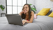 Young beautiful hispanic woman using laptop lying on bed at bedroom