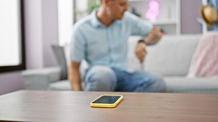 Wall Mural - A man wearing a blue shirt checks his watch in a modern living room with a smartphone on the table.