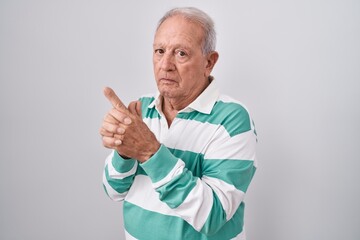 Wall Mural - Senior man with grey hair standing over white background holding symbolic gun with hand gesture, playing killing shooting weapons, angry face