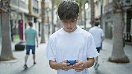 Young caucasian male teenager focused on smartphone on a bustling city street.