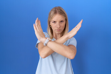 Poster - Young caucasian woman wearing casual blue t shirt rejection expression crossing arms doing negative sign, angry face