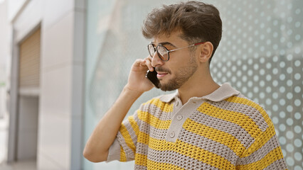 Canvas Print - Handsome arabian man, chilling under the city sun, deeply engrossed in a serious phone conversation on his trendy smartphone, standing on a busy street surrounded by urban vibes.