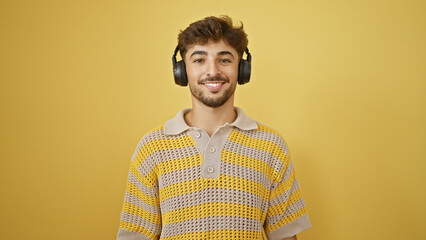 Sticker - Smiling young arab man coolly enjoying music, listening with headphones on, exuding confidence over an isolated yellow background