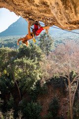 Wall Mural - Girl climber on an overhanging rock. A sports woman climbs a rock against the backdrop of mountains. difficult movements in rock climbing.