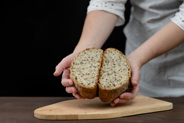 Woman demonstrating a cut  into two halves fresh whole grains warm bread on dark background