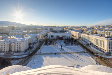 Wall Mural - City of Magadan, Magadan region, Russia. View from the roof of the snow-covered Cathedral Square, streets and buildings. Bright sunlight. View from the bell tower of the Holy Trinity Cathedral.