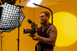 © Big Shot Theory - Man holding a camera in front of yellow background
