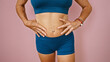 A fit middle-aged woman touches her toned abdomen against a pink background, implying health and wellness.