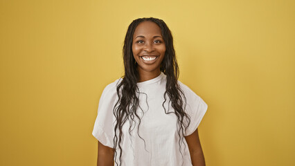 Wall Mural - Portrait of a smiling young adult african american woman with curly hair against a yellow isolated background.