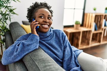 Wall Mural - African american woman talking on the smartphone sitting on sofa at home