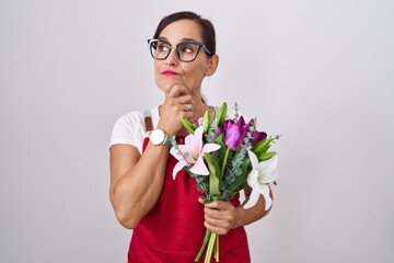 Sticker - Middle age brunette woman wearing apron working at florist shop holding bouquet with hand on chin thinking about question, pensive expression. smiling with thoughtful face. doubt concept.