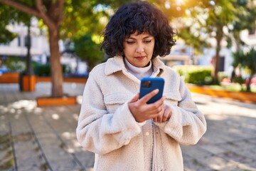 Wall Mural - Young beautiful hispanic woman using smartphone with serious expression at park