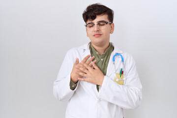 Poster - Young non binary man wearing doctor uniform and stethoscope smiling with hands on chest with closed eyes and grateful gesture on face. health concept.