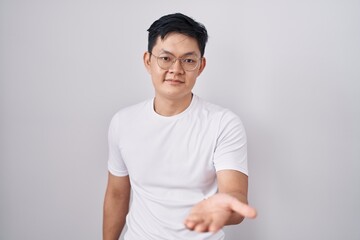 Sticker - Young asian man standing over white background smiling cheerful offering palm hand giving assistance and acceptance.