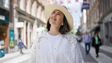 Beautiful young hispanic woman smiling confident looking to the side wearing summer hat in the streets of Stockholm