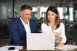 © Stock 4 You - Team of diverse partners sitting at table mature Latin business man and European business woman discussing project on tablet in office. Two colleagues of professional business people working together.