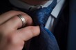 closeup of a hand fixing a tie, with an engraved silver ring