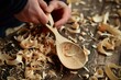person carving a wooden spoon by hand with wood shavings around