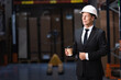 pleased middle aged businessman in hard hat and suit holding coffee in warehouse, professional