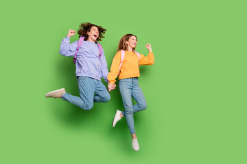 Poster - Full length portrait of delighted two people hold arms jump raise fists empty space ad isolated on green color background