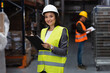 © LIGHTFIELD STUDIOS - happy warehouse worker in safety vest and hard hat writing on clipboard, logistics and distribution