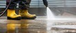 A person wearing yellow rubber boots uses a powerful water jet to diligently clean the outdoor floor.