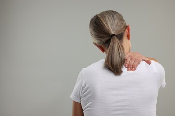 Sticker - Mature woman suffering from pain in her neck on grey background, back view. Space for text