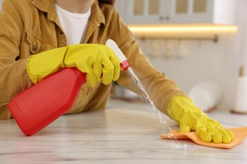 Sticker - Woman with spray bottle and microfiber cloth cleaning white marble table in kitchen, closeup